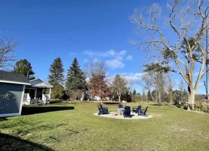 Outdoor fire pit area with blue chairs, surrounded by trees and a clear blue sky.