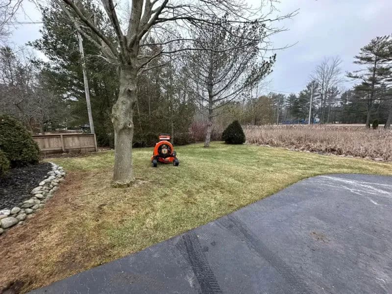 Person mowing a lawn with a riding mower in a residential yard on a cloudy day.