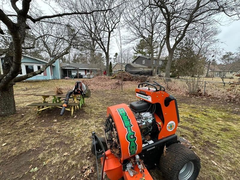 Lawn care equipment parked in a yard with leaf piles and trees, showcasing outdoor maintenance.