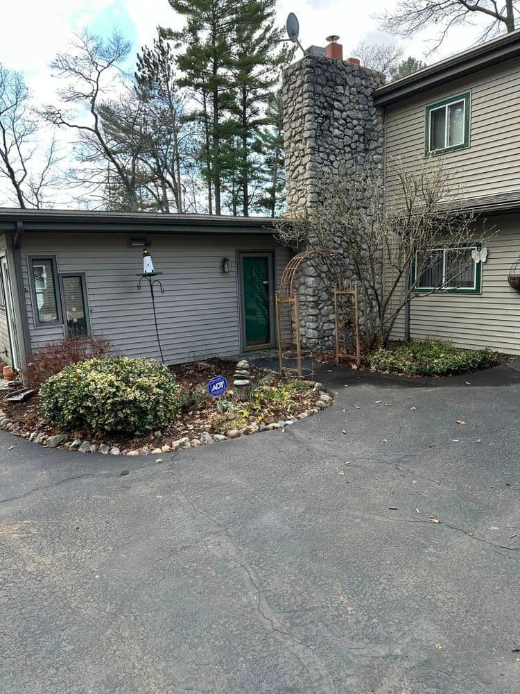 Home exterior featuring a stone chimney, landscaped front yard, and driveway.