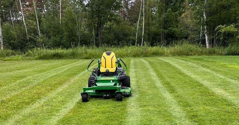 Lawn mower on freshly mowed grass with clear stripes in a wooded area.