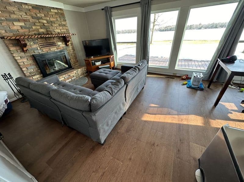 Cozy living room with gray sectional sofa, brick fireplace, large windows, and lake view.