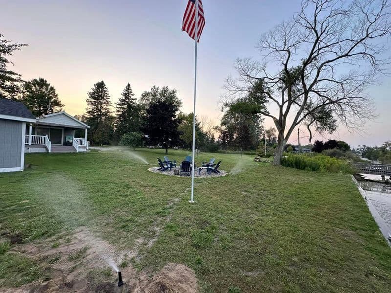 American flag stands by lake with chairs around fire pit in scenic outdoor setting.