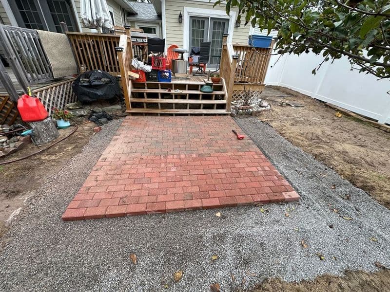 Paved patio area with red bricks and gravel, surrounded by a wooden deck and garden space.